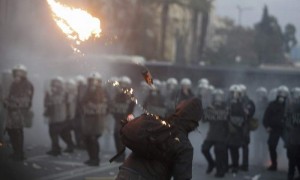 Un manifestante lanza un coctel molotov contra la policía, durante las protestas por los acuerdos de la troika, en Atenas. Más de cien mil personas se manifestaron en contra de las medidas exigidas por la troika, en una protesta que fue reprimida duramente por la policía con el uso de gases lacrimógenos. Desde primera hora de la tarde miles de personas bloquearon el centro de Atenas para manifestar su desacuerdo contra el pacto entre el gobierno y la troika, la tríada formada por el Fondo Monetario Internacional (FMI), el Banco Central Europeo (BCE) y la Unión Europea (UE). Foto: Simela Pantzartzi / Efe