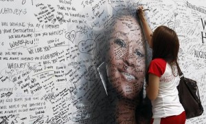 Una joven firma un mural con la fotografía de la cantante estadounidense Whitney Houston, en un centro comercial en Quezón al este de Manila (Filipinas), este viernes, 17 de febrero de 2012. Foto: Dennis M. Sabangan / Efe